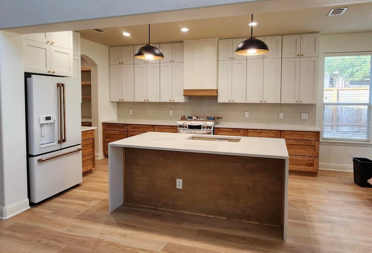 Modern kitchen with white cabinets, island, stainless fridge, and two pendant lights