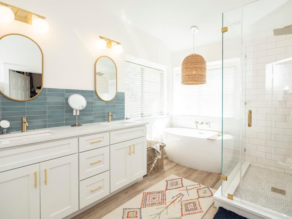 Bright modern bathroom with white vanity, blue tile backsplash, round mirrors, freestanding tub, and glass shower.
