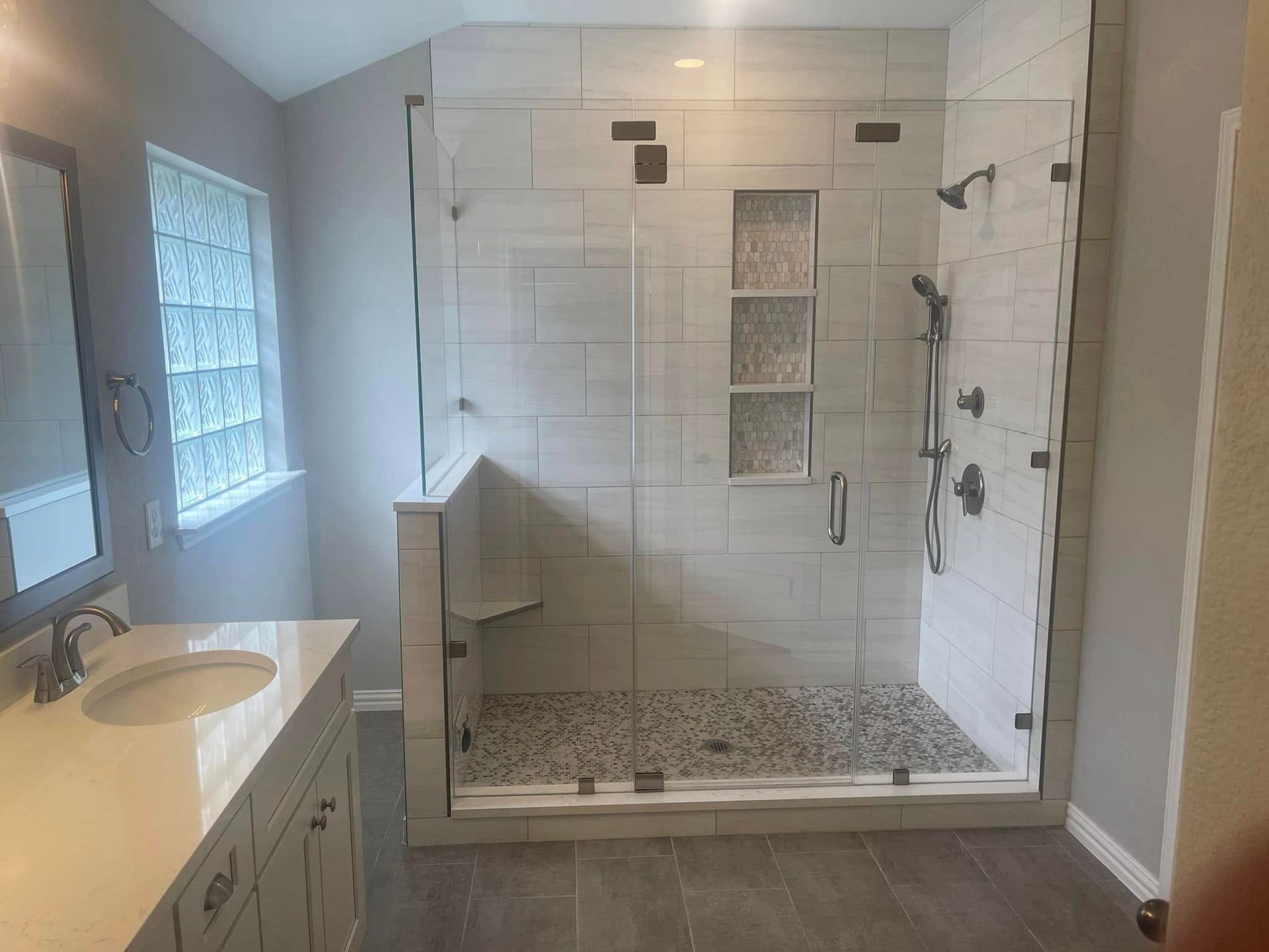 Bathroom with walk-in shower, white tile, glass door, and vanity beside a window.