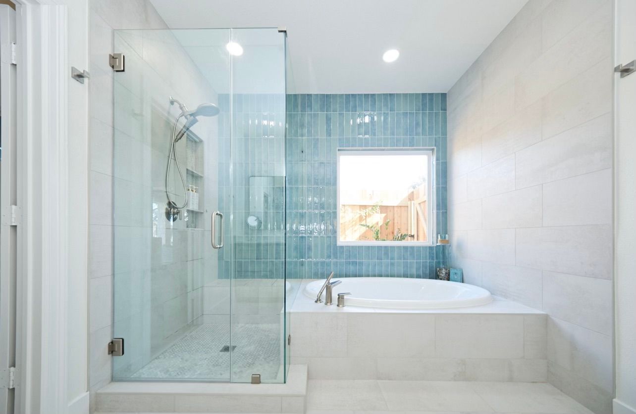 Bright modern bathroom with a glass shower, white tub, and blue tile accent wall