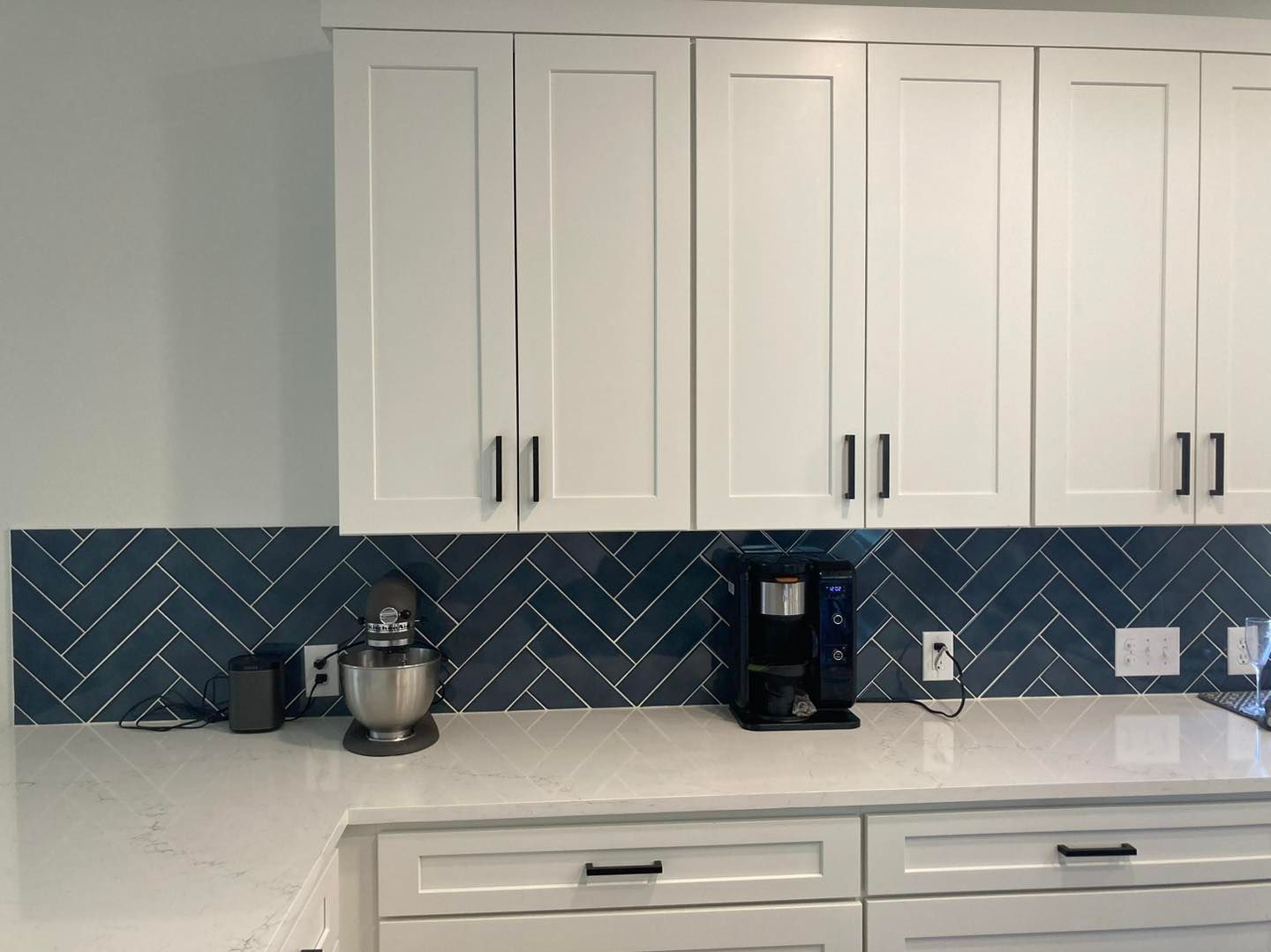 Modern kitchen with white cabinets, blue herringbone backsplash, and coffee maker on the counter