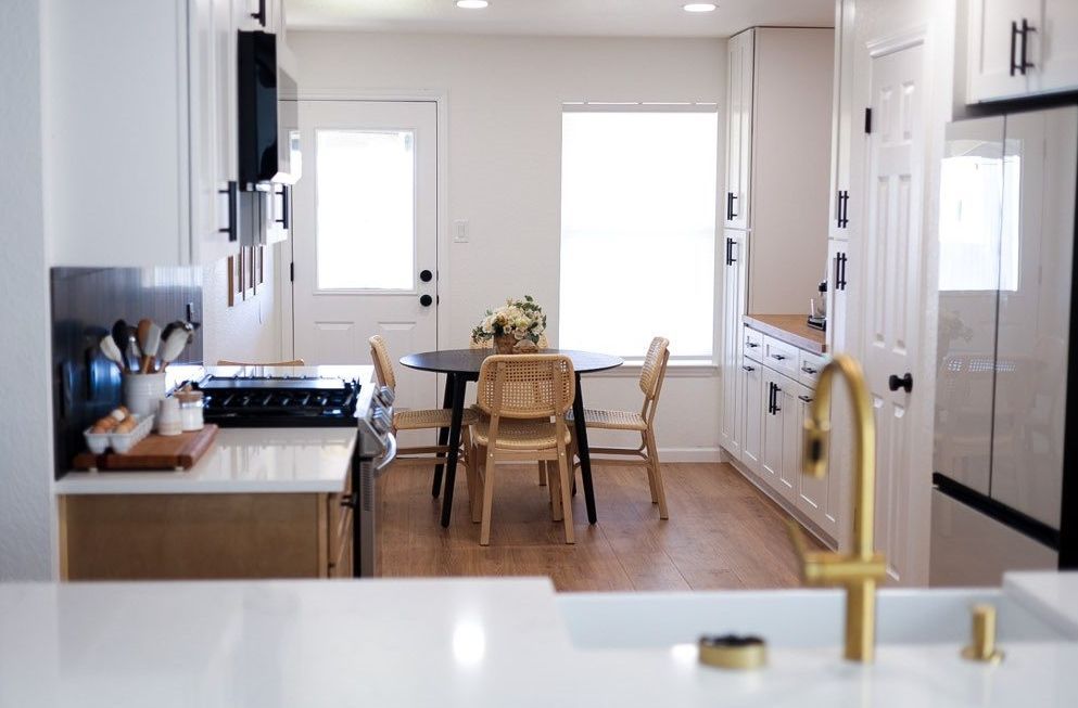 Bright, modern kitchen with white cabinets, wood floor, and a dining table by the window.