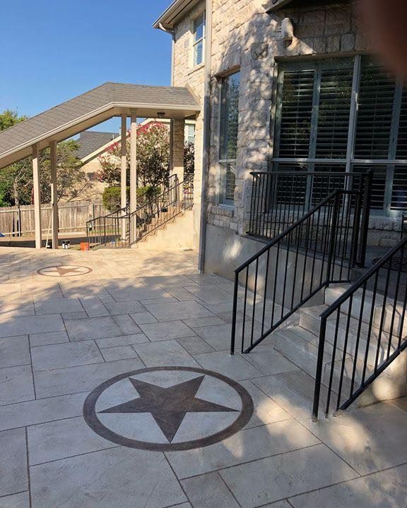 Stone patio with a circular star emblem beside a house and metal staircase handrail.