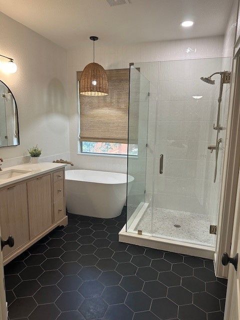 Modern bathroom with black hex tile floor, freestanding tub, glass shower, and wood vanity