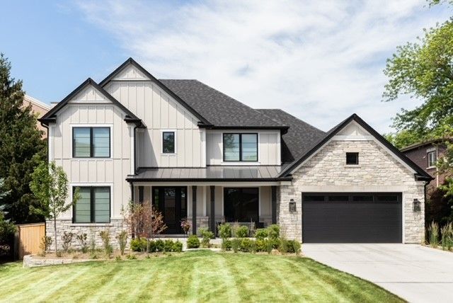 Modern two-story house with white siding, stone facade, black garage door, and a manicured lawn