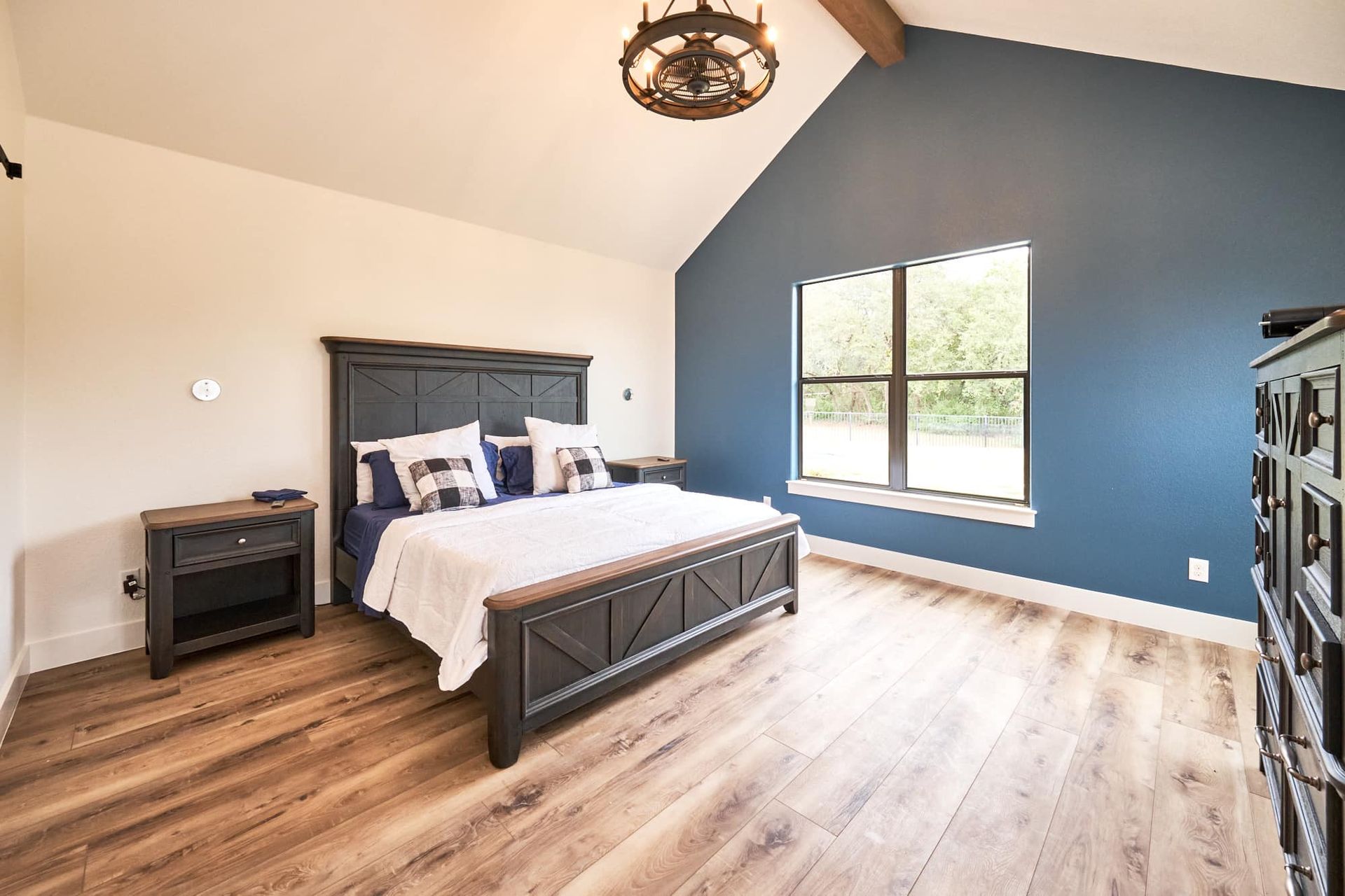 Bright bedroom with a dark wood bed, blue accent wall, and large sunlit window.