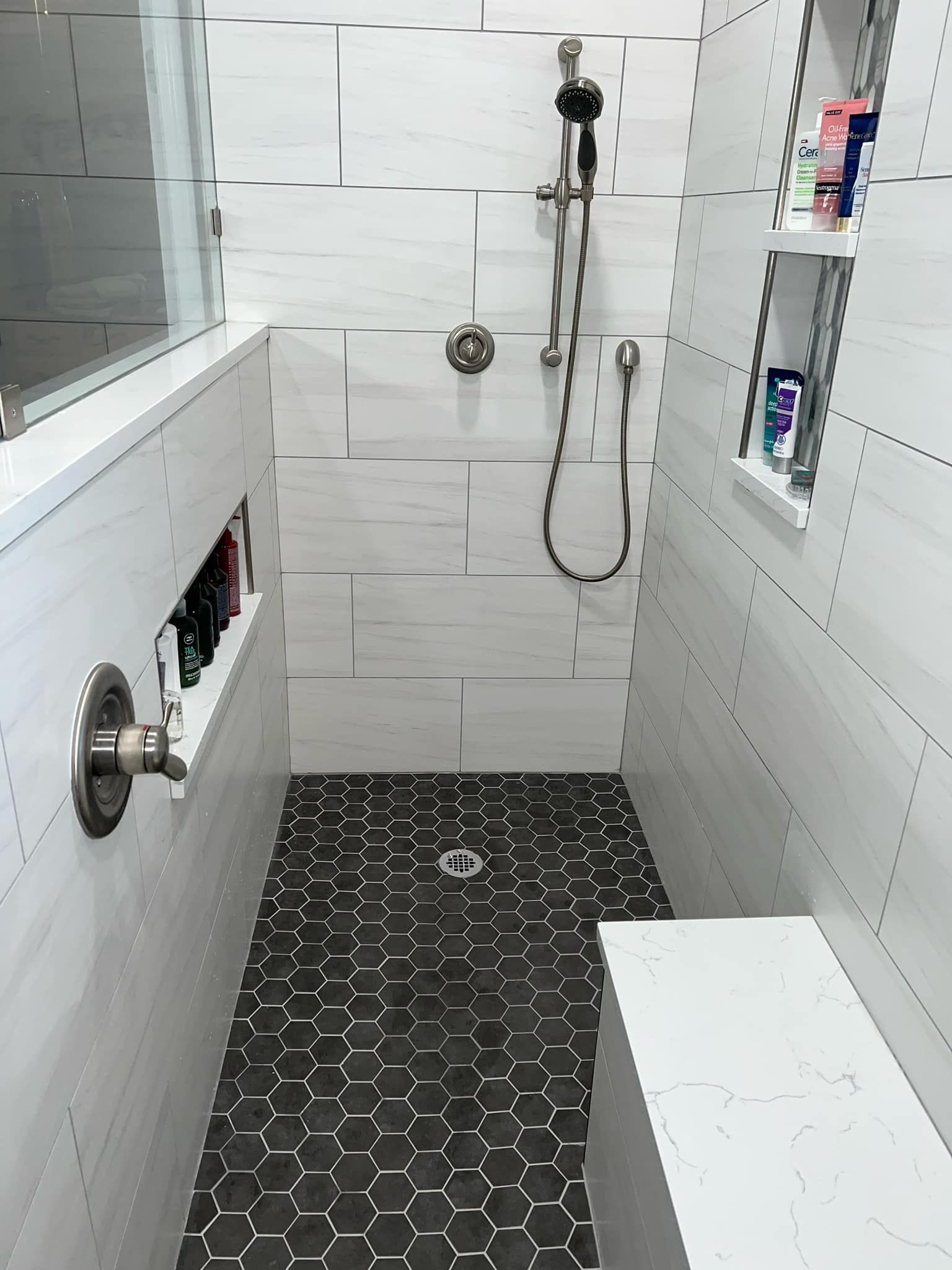 White-tiled shower with chrome fixtures, wall niches, and dark mosaic floor tiles.