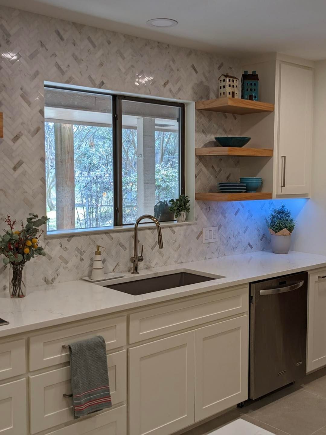 Modern kitchen with white cabinets, marble backsplash, window over sink, and open wood shelves.