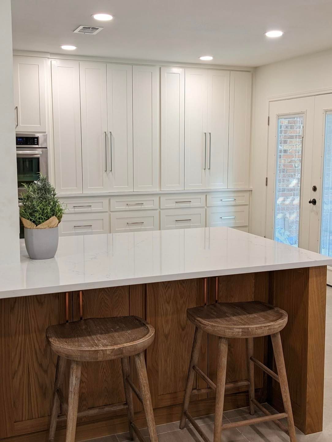 Bright white kitchen with island, two wooden stools, built-in cabinets, and a glass door.