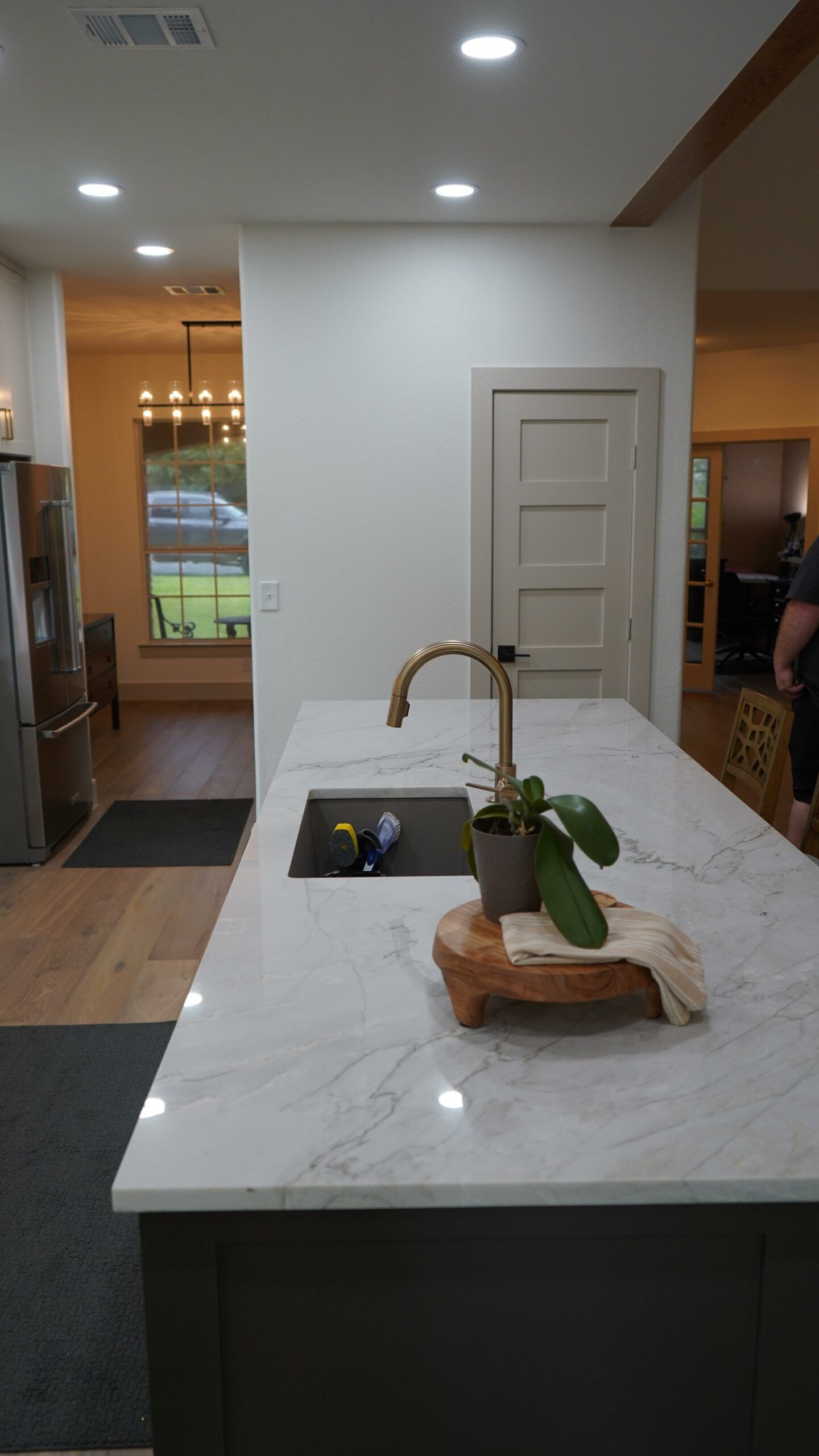 Modern kitchen island with marble counter, brass faucet, and potted plant in a bright open-concept home
