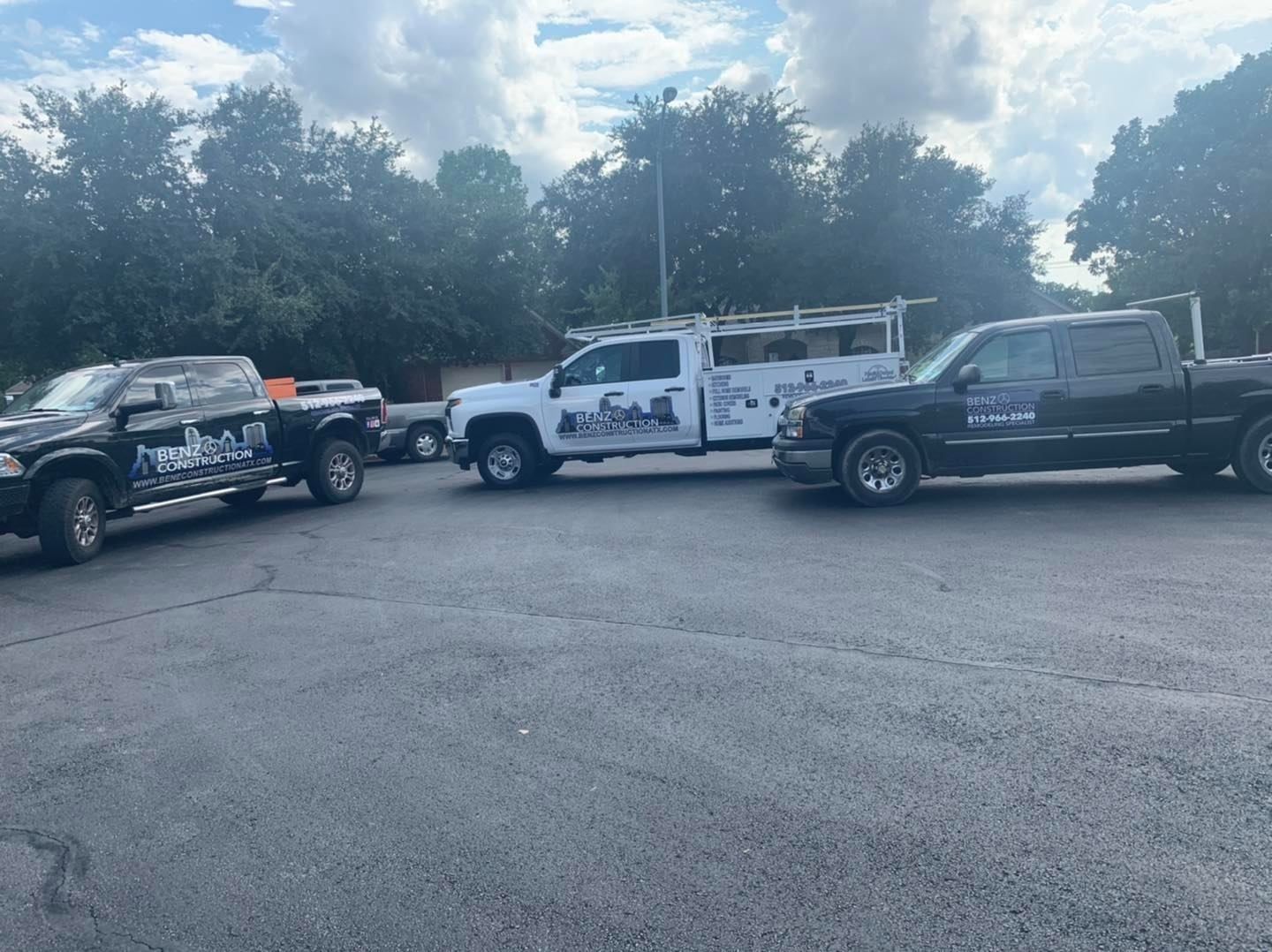 Parked work trucks and utility vehicles in a gravel lot under cloudy skies