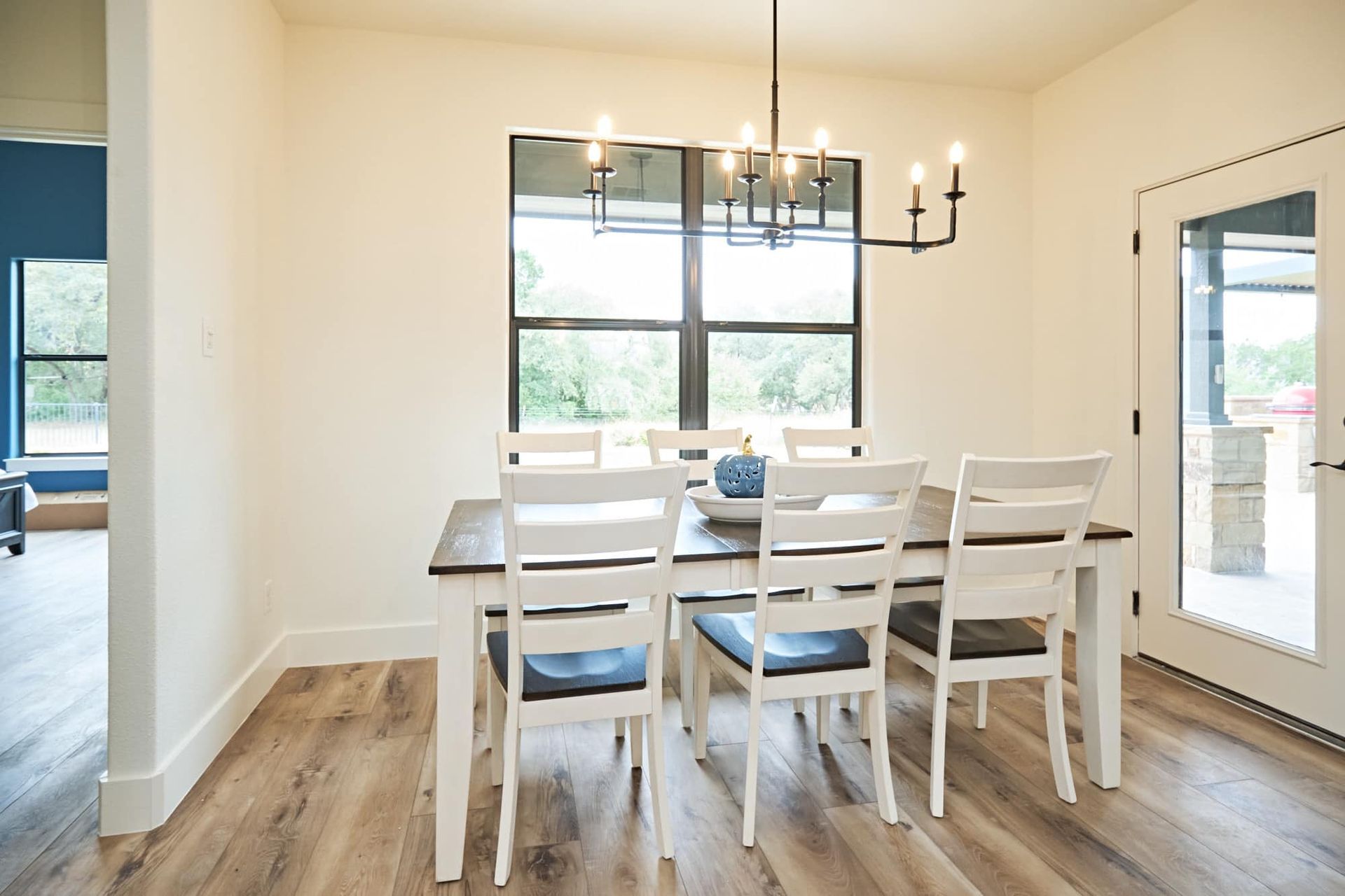 Bright dining room with white table, chairs, black chandelier, and large windows on wood floors