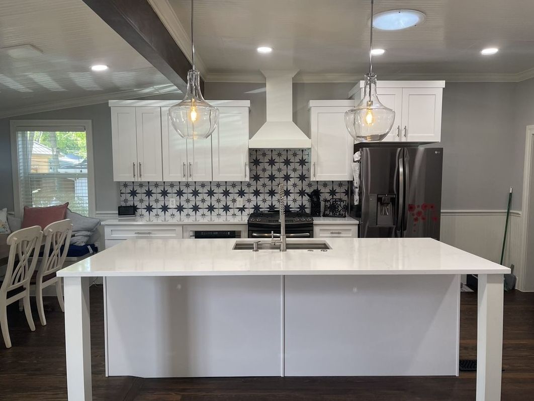 Modern white kitchen with island, pendant lights, black range hood, and tiled backsplash