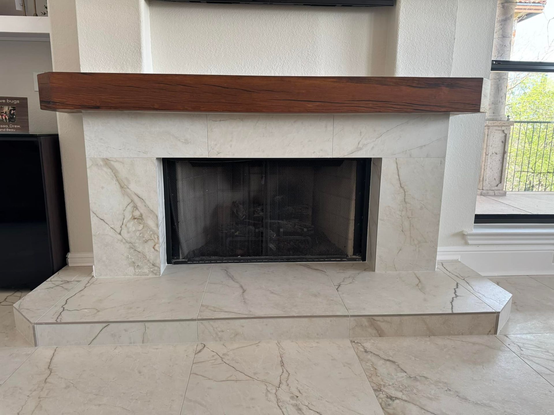 White stone fireplace with a dark wood mantel and large hearth in a bright living room