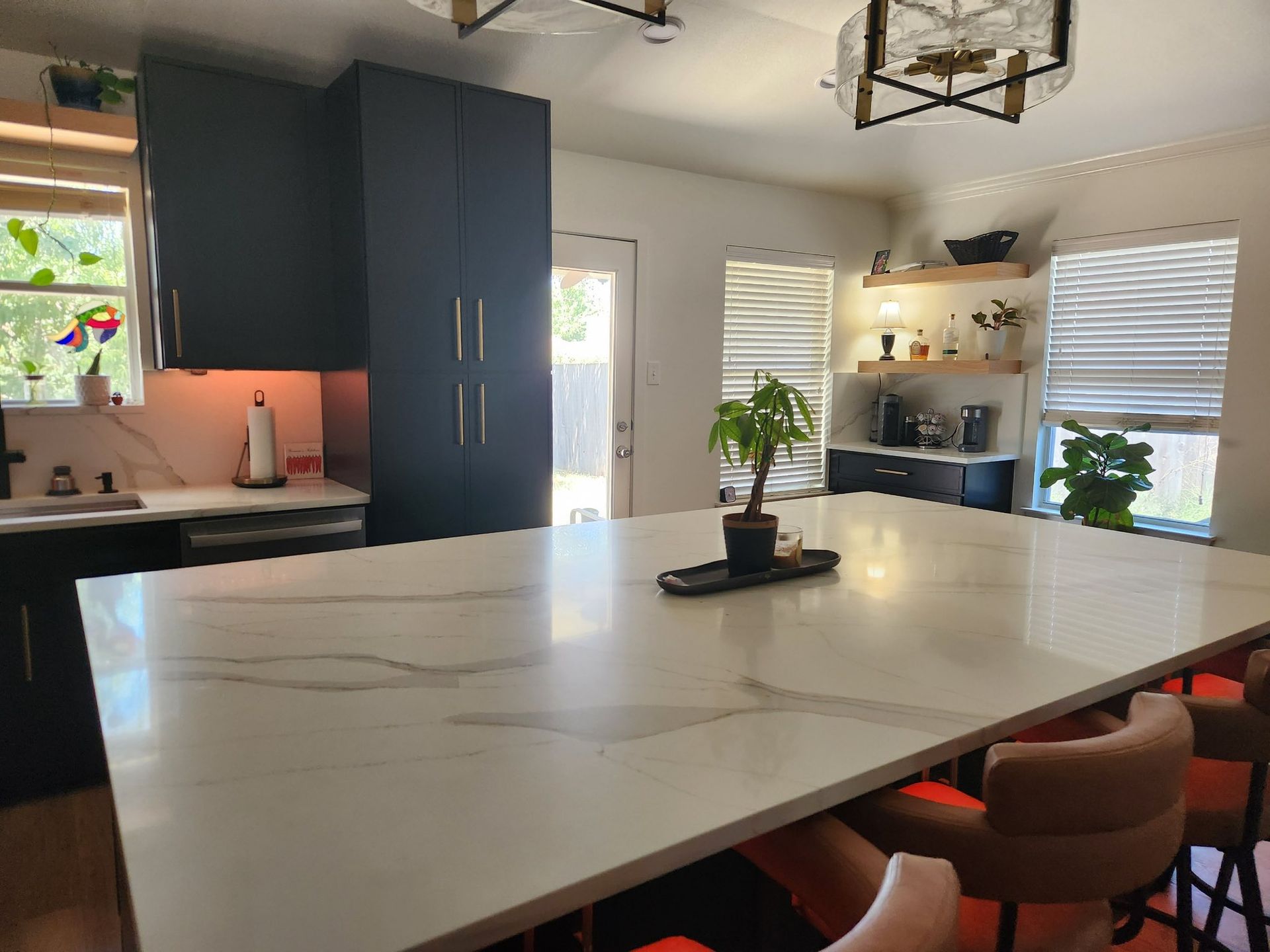 Modern kitchen with large island, dark cabinets, and warm chairs by the counter