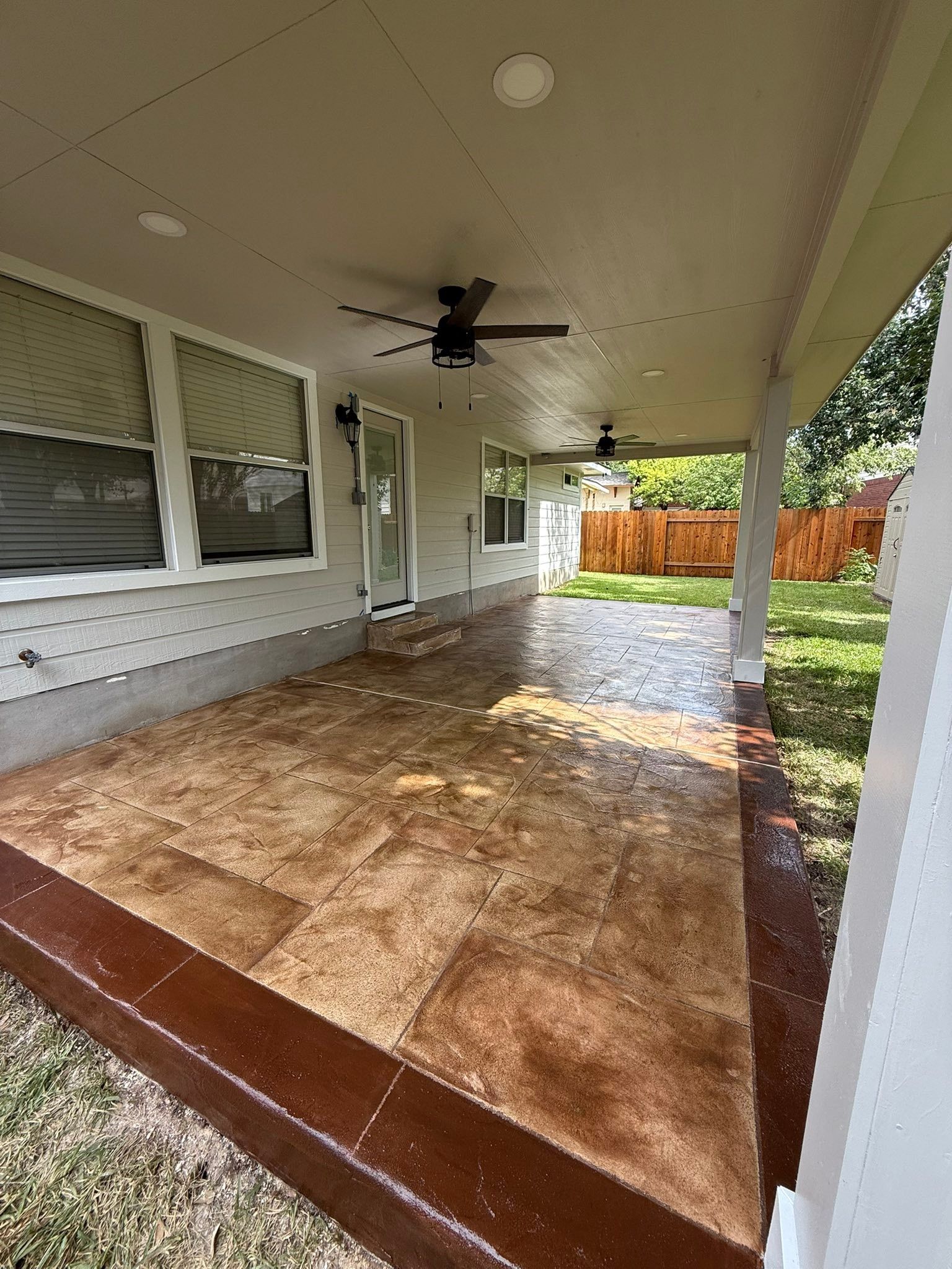 Covered patio with a ceiling fan, tiled floor, windows, and a fenced backyard beyond.