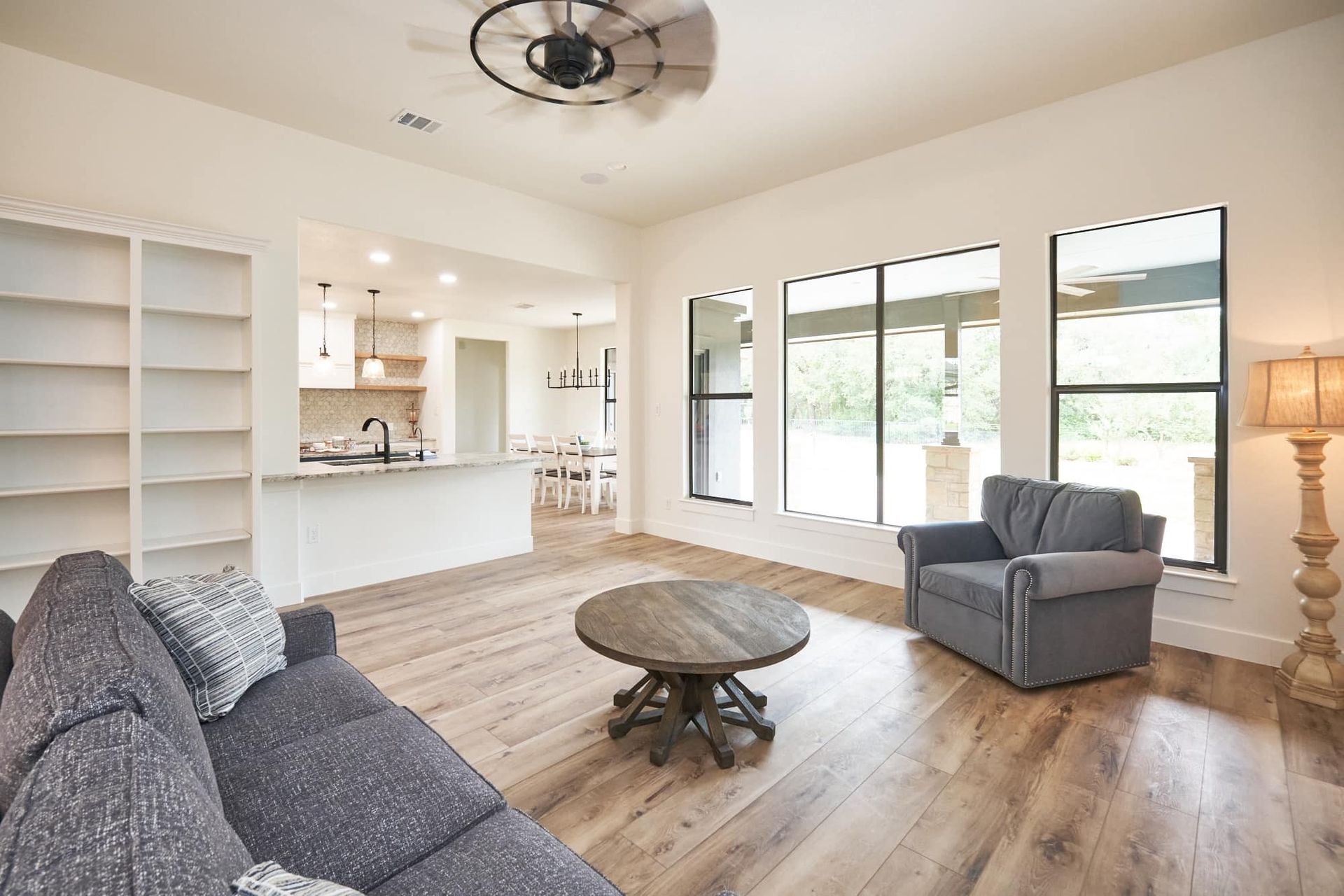 Bright open living room with gray sofas, round coffee table, large windows, and wood floors