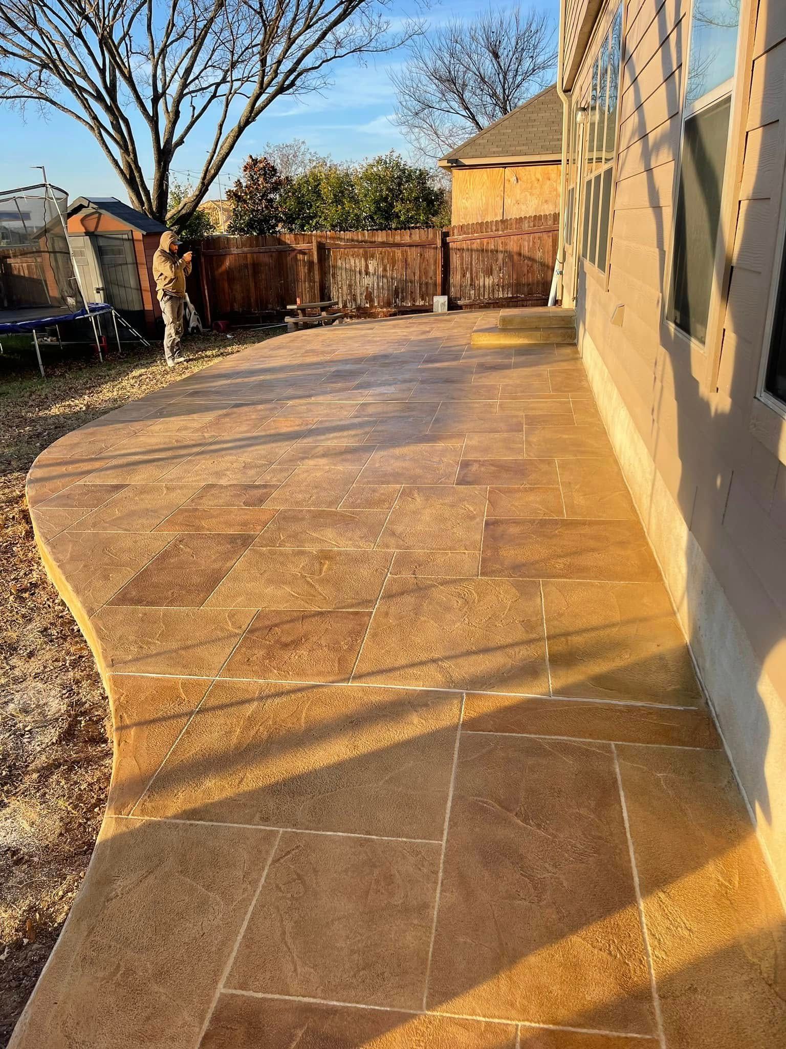 Sunlit stone patio beside a house, with a wooden fence and bare trees in the yard.