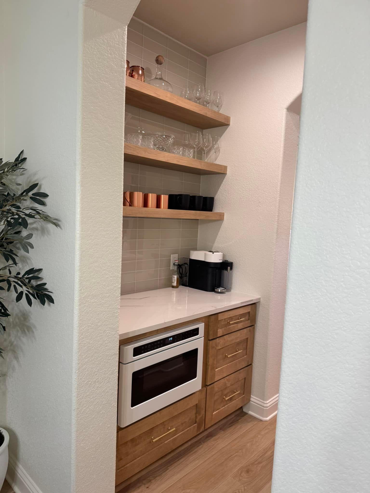 Small kitchen nook with built-in oven, wood drawers, open shelves, and coffee maker.