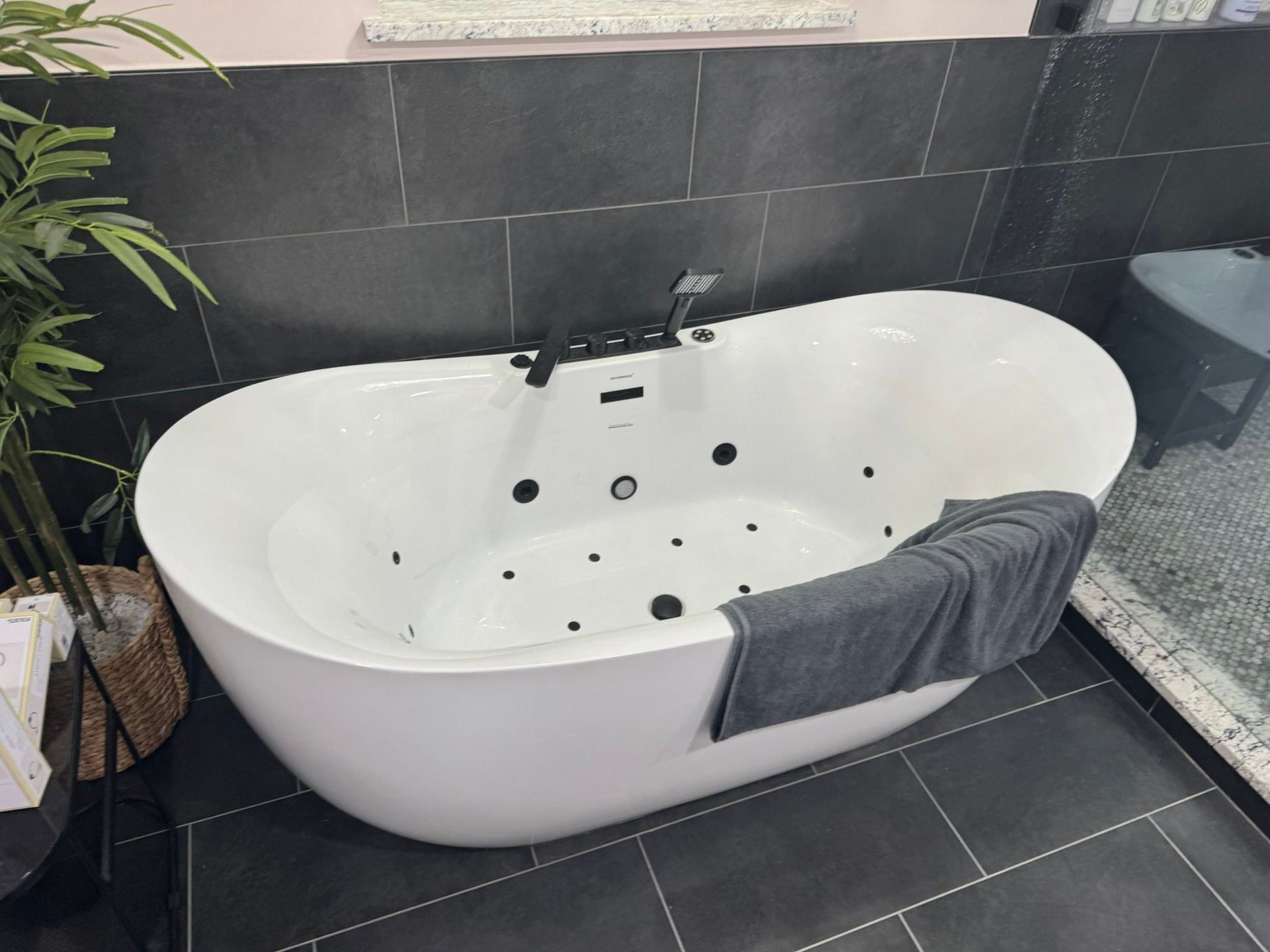 White freestanding bathtub with black tile surround and a gray towel draped over the side