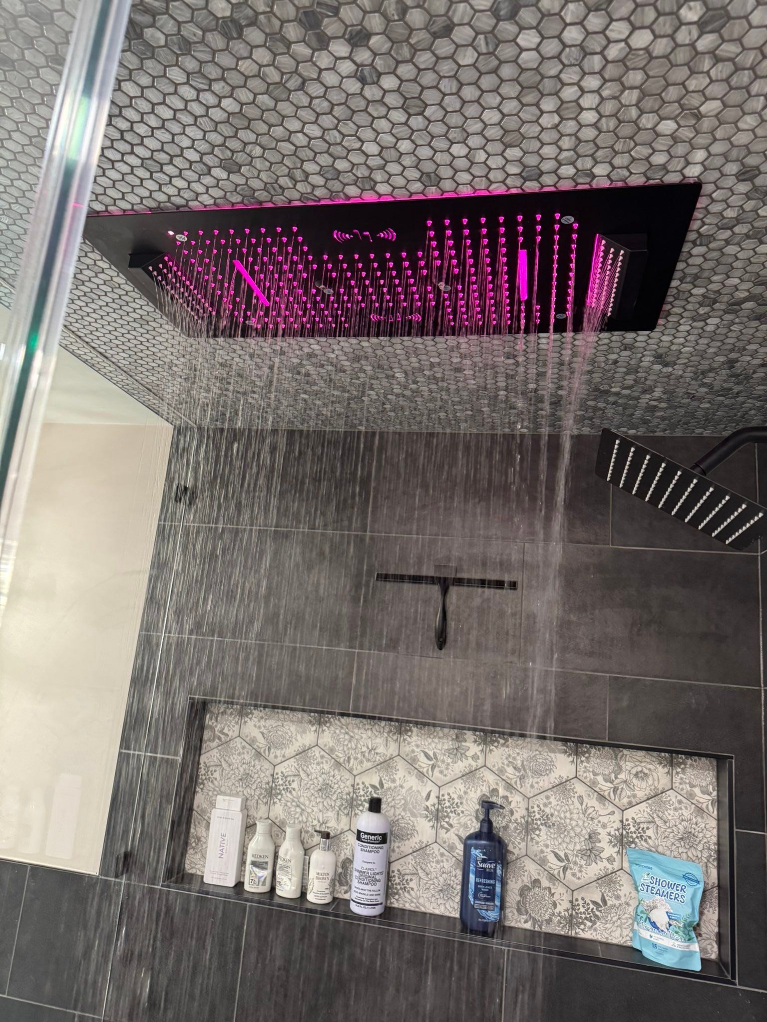 Modern black shower with rainfall head and magenta LED ceiling light over tiled walls