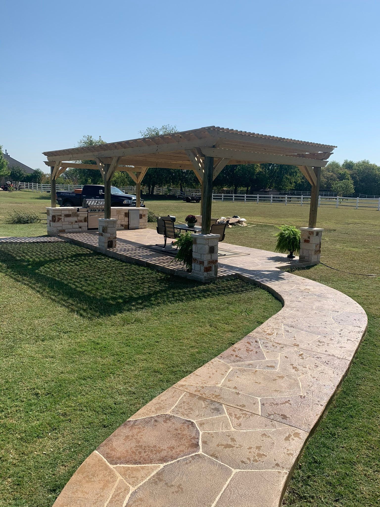 Stone path leading to a shaded picnic pavilion in a grassy park under a clear blue sky