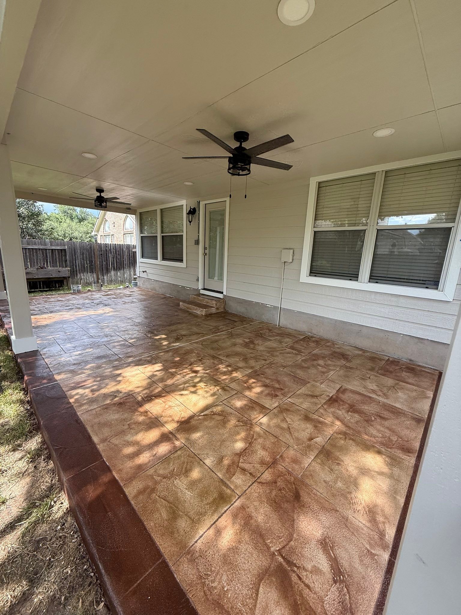 Covered patio with patterned tile floor, ceiling fan, and white siding windows and door.