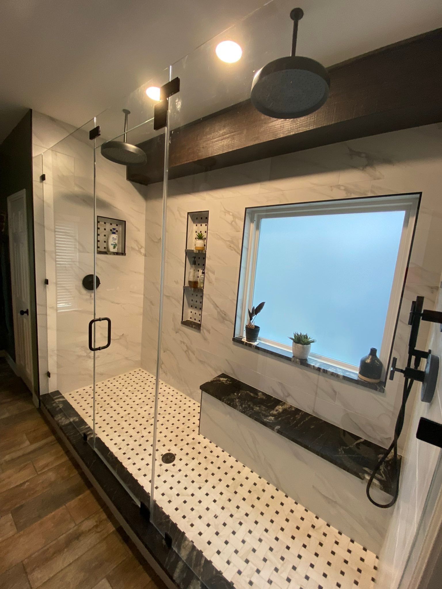 Modern bathroom with white tile shower, black fixtures, and frosted window shelf with plants