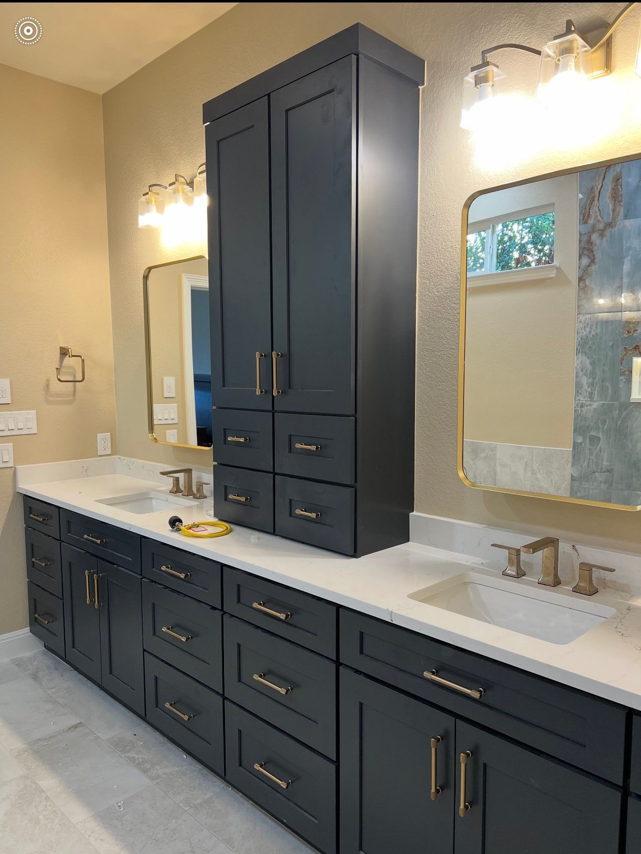 Modern bathroom with dark navy cabinets, white countertop, and lit mirror above the sink.