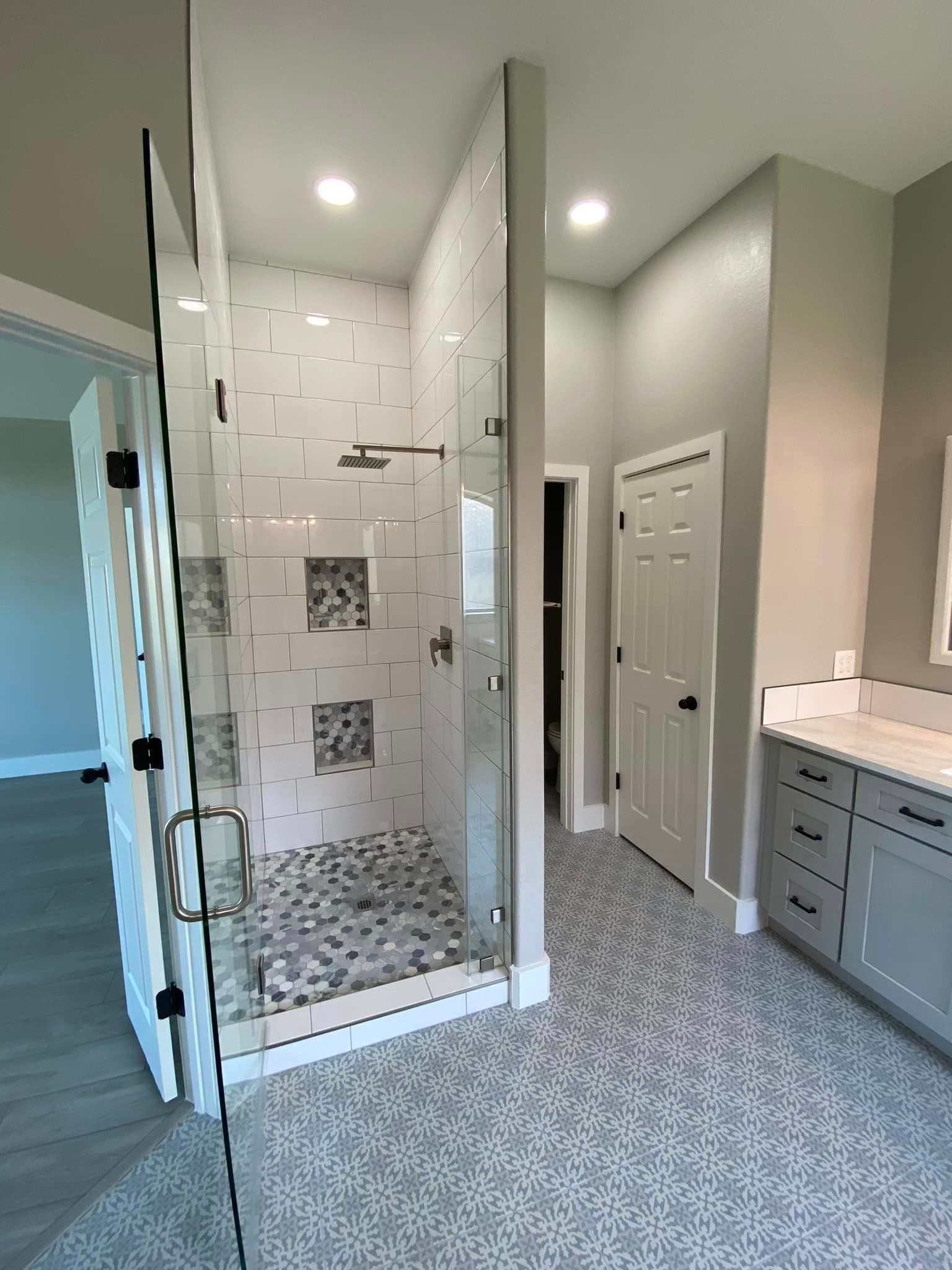 Modern bathroom with glass shower, gray tile floor, and white vanity cabinets