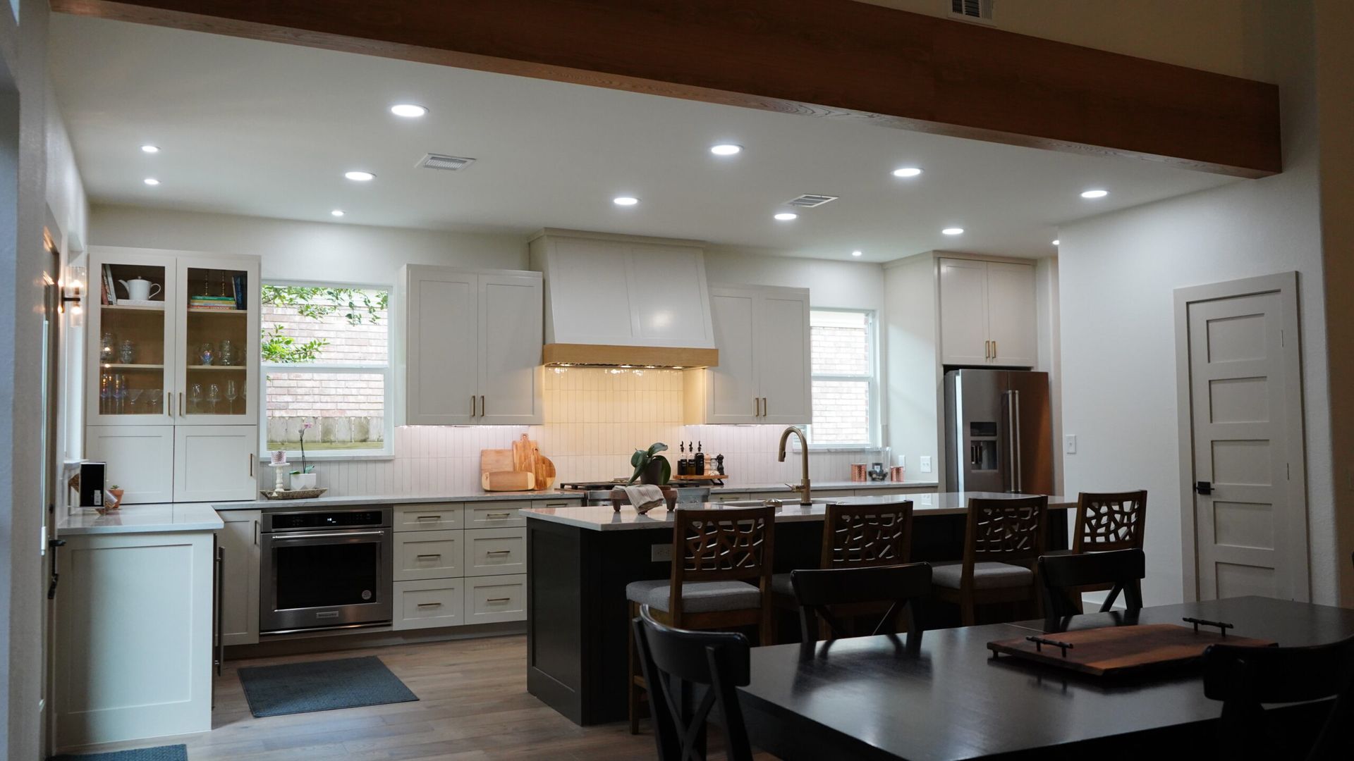 Modern open-concept kitchen and dining area with white cabinets, island, pendant lights, and dark wood accents