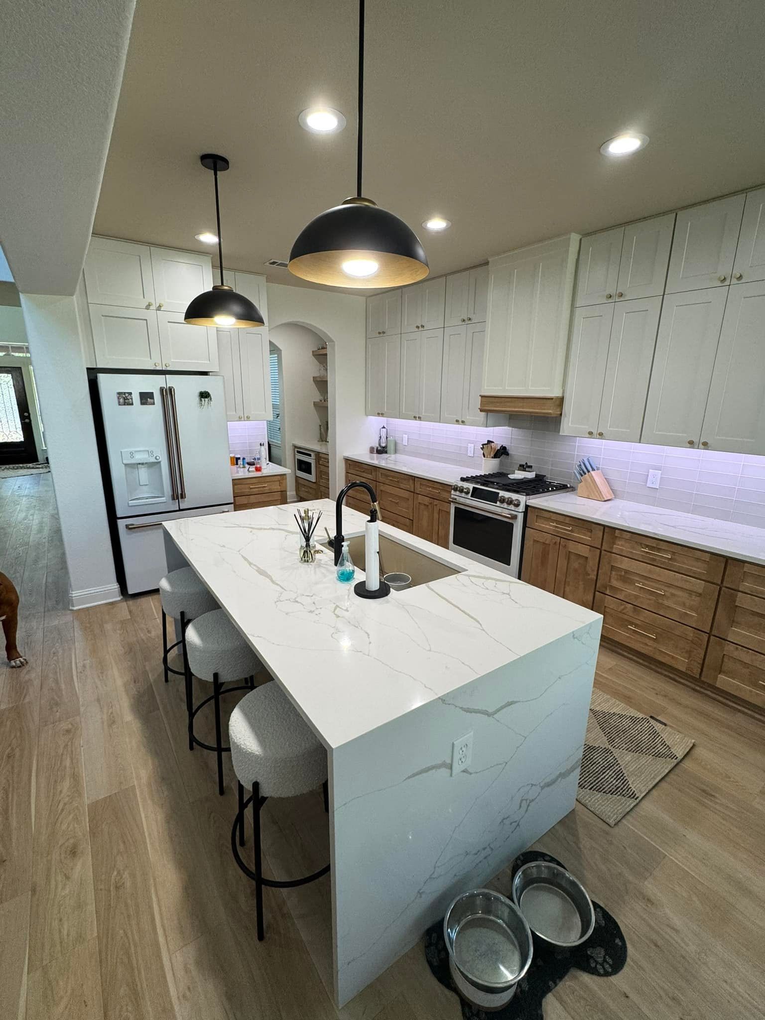 Modern kitchen with white island, black pendant lights, wood cabinets, and stainless steel appliances