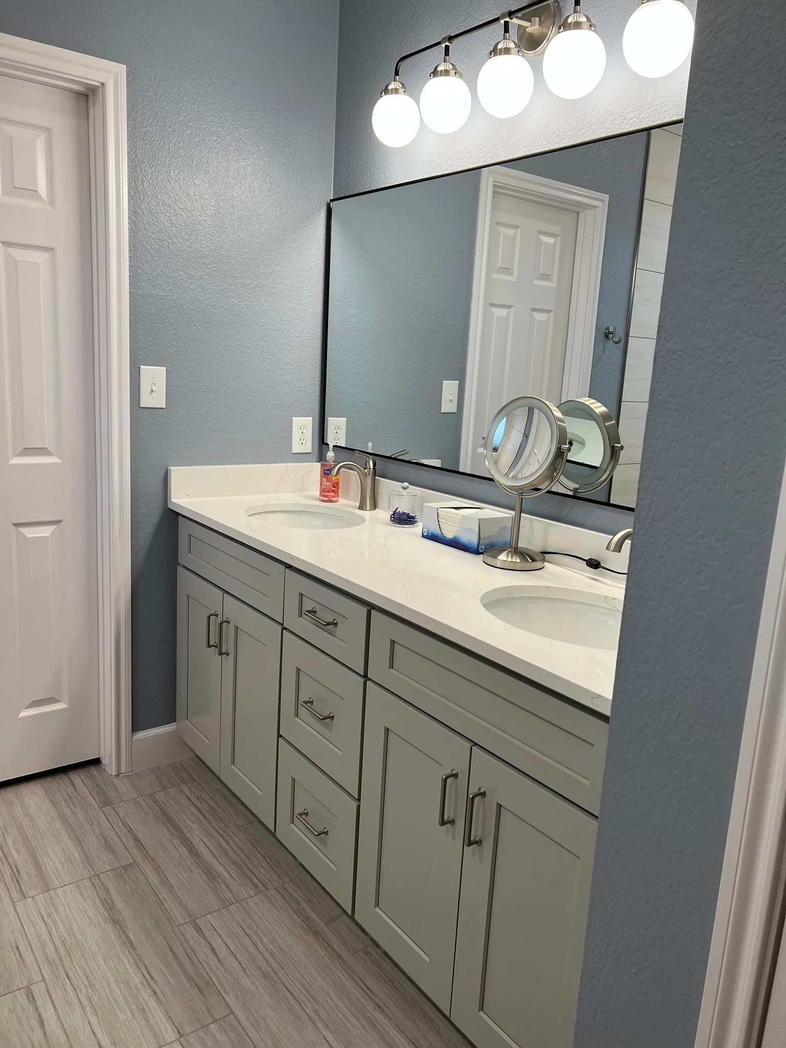 Modern bathroom vanity with gray cabinets, white countertop, large mirror, and bright vanity lights.