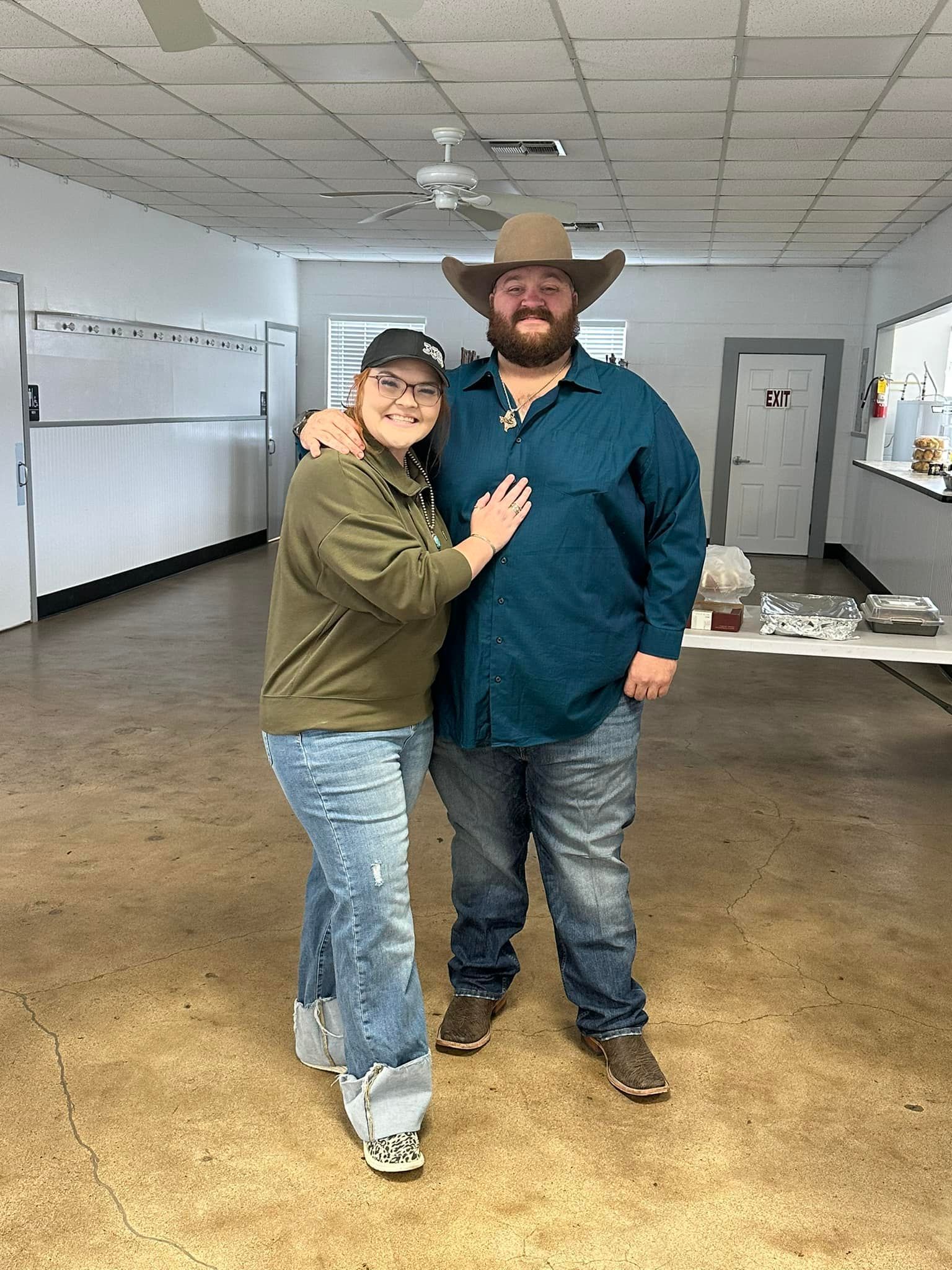Two people standing in a room, smiling and posing together, one in a cowboy hat.