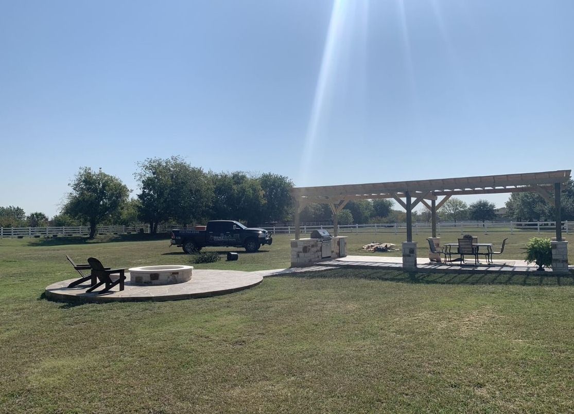 Sunny park picnic area with shaded tables, benches, and parked trucks on a grassy field