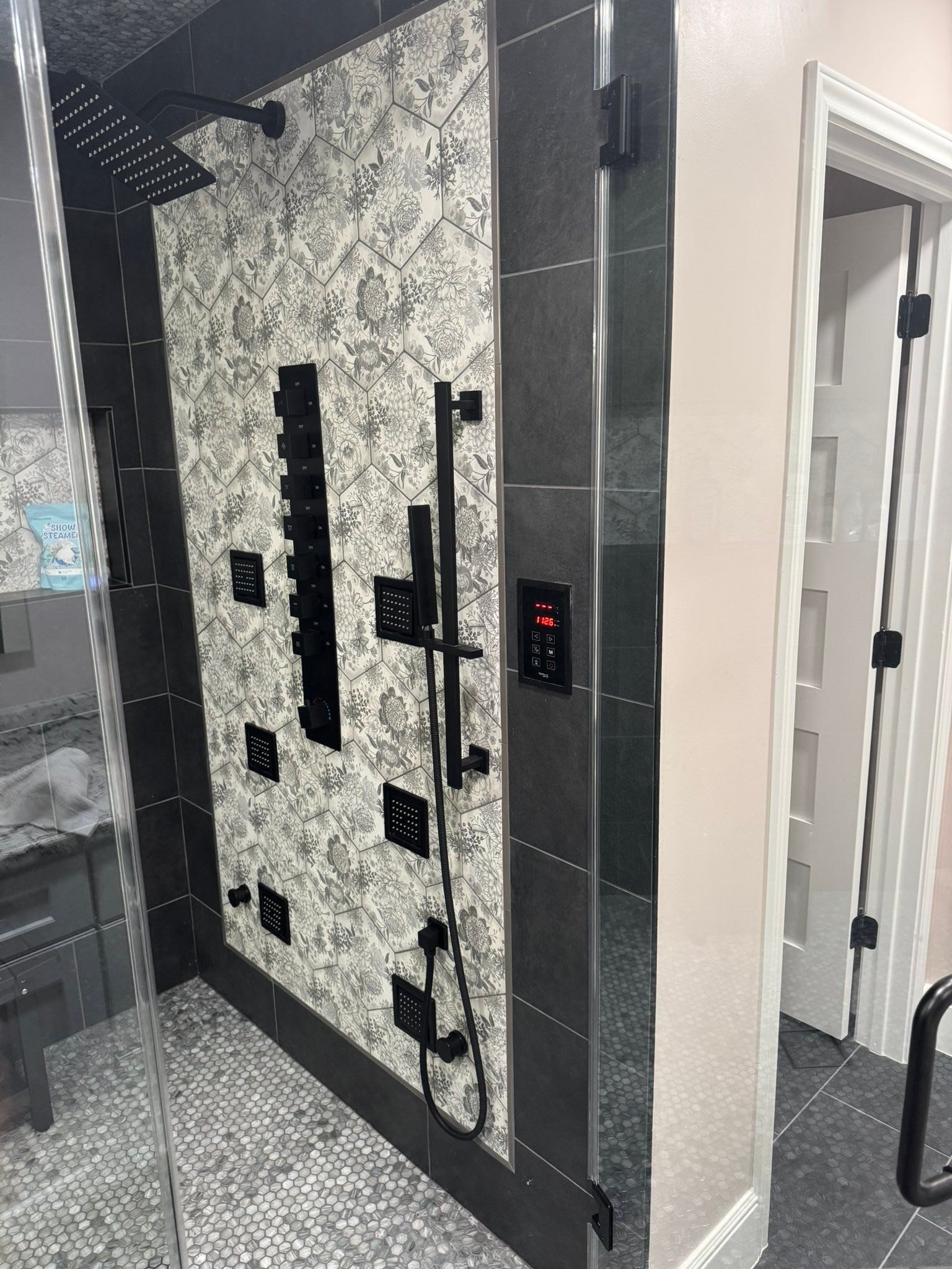 Modern shower entrance with patterned tile, black trim, and a wall-mounted control panel