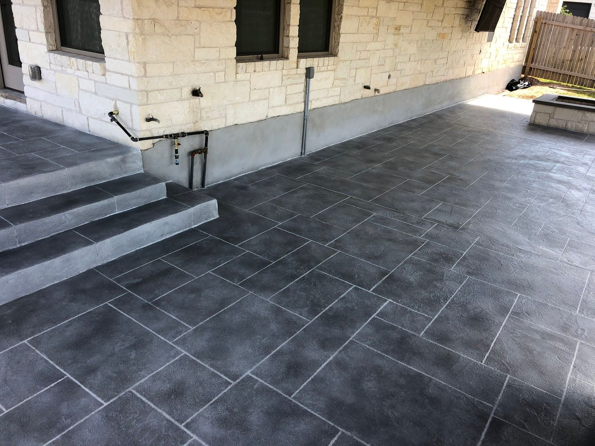 Stone patio beside a house with steps, dark tiled floor, and windows on the wall