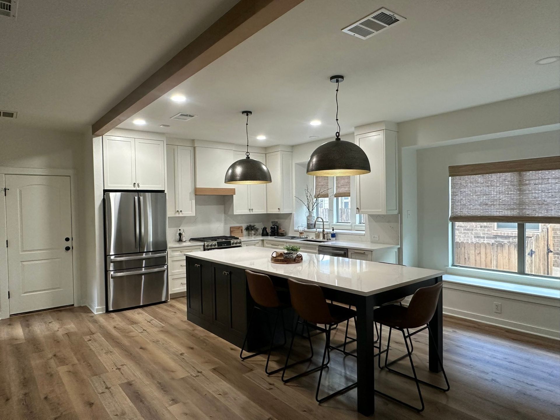 Modern kitchen with island, pendant lights, stainless fridge, and large window seat nook.