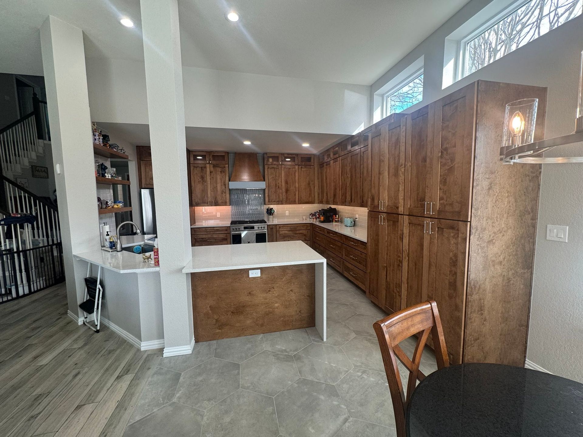 Open kitchen with wood cabinets, white island, and high windows in a bright dining area