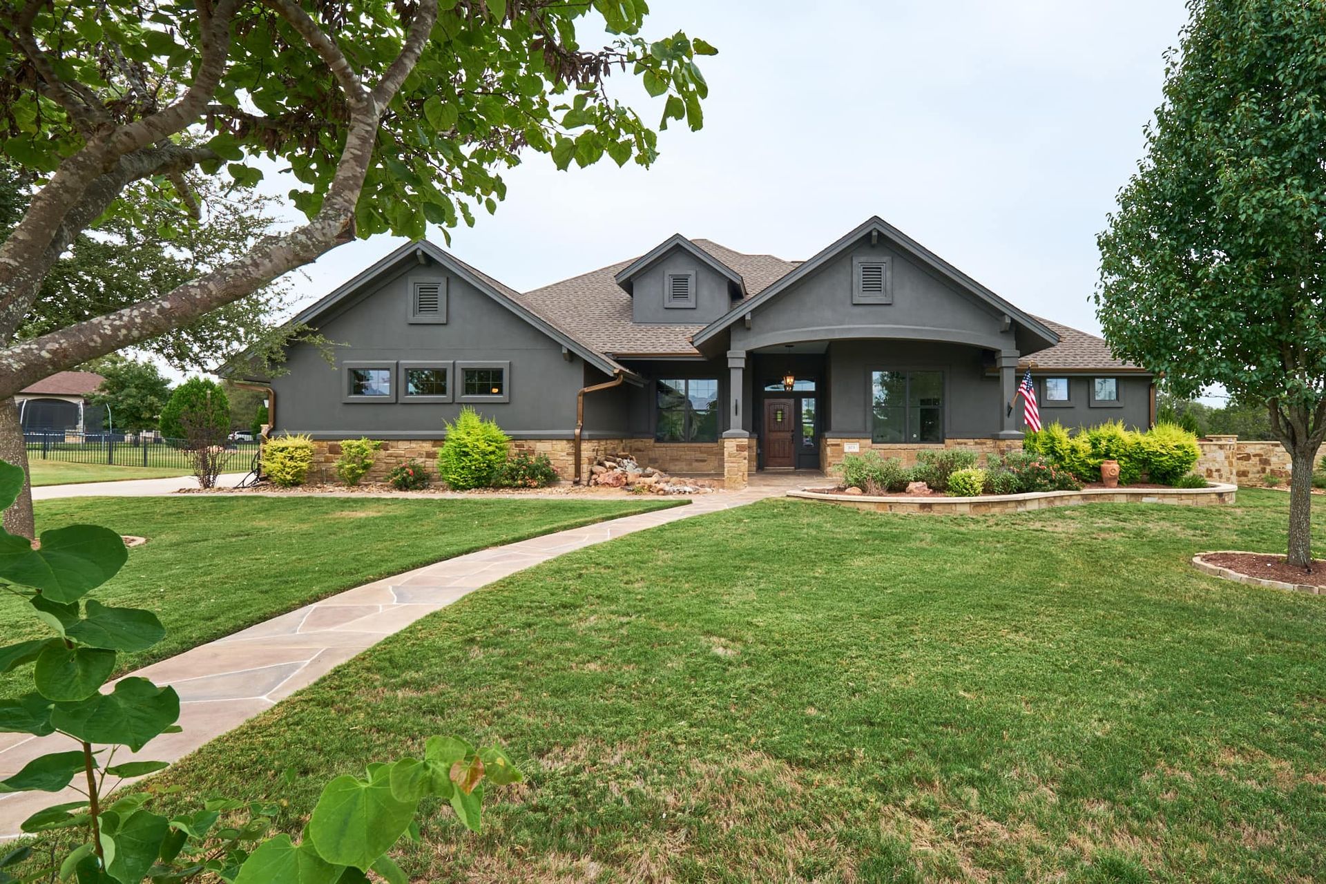 Modern gray house with a stone walkway, landscaped front yard, and large trees