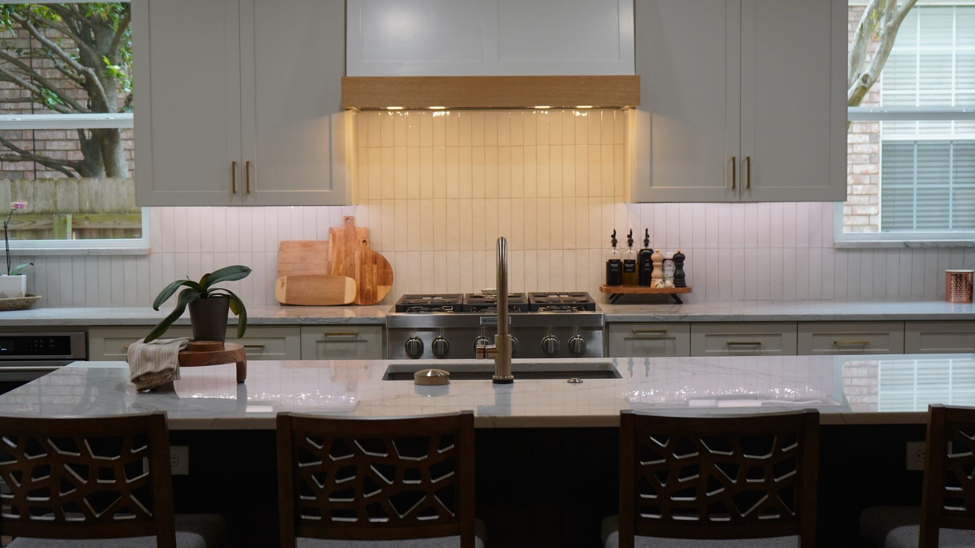 Bright modern kitchen with a large island, sink, dark stools, and warm under-cabinet lighting