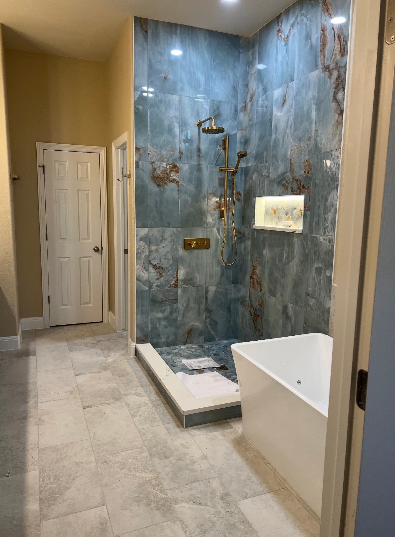 Modern bathroom with blue stone shower wall, white tub, and beige tiled floor