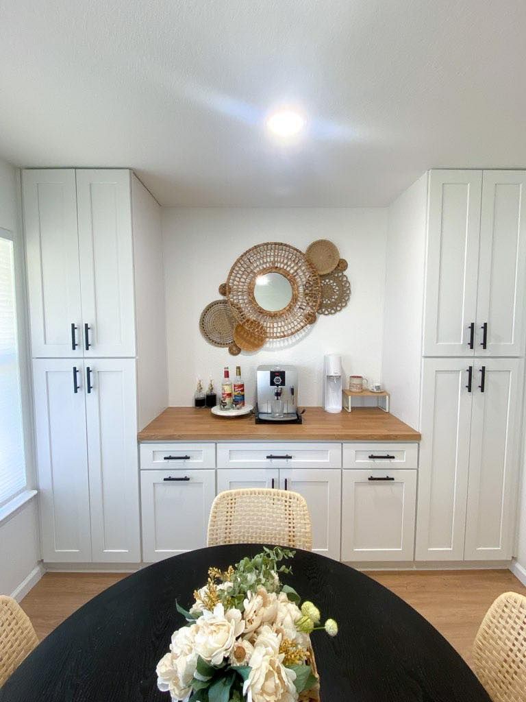 Bright dining room with built-in white cabinets, wooden countertop, woven wall decor, and a round table centerpiece.
