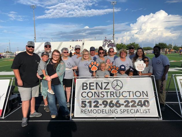 Group holding a BENZ Construction banner on a sunny outdoor field.