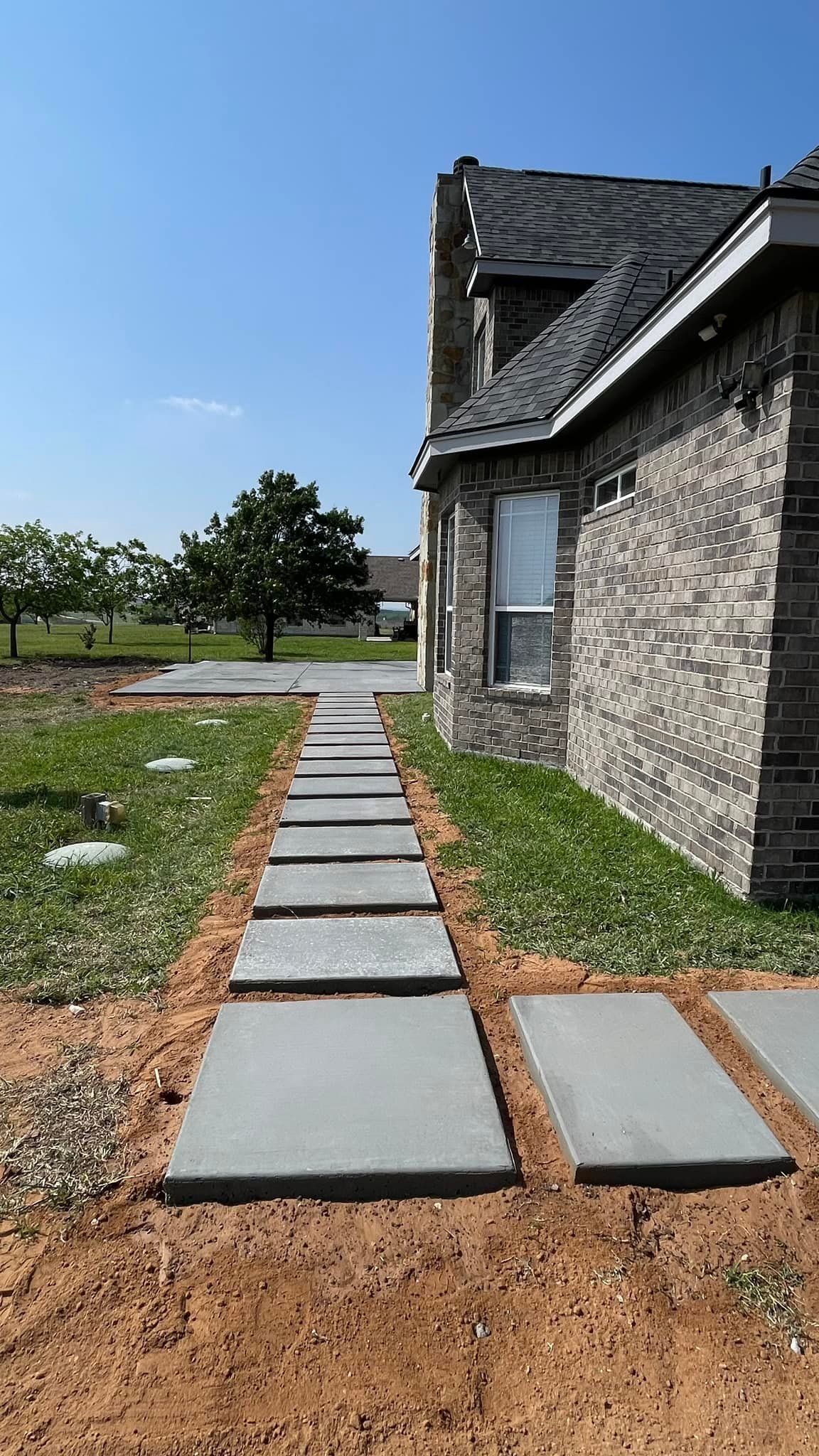 Stone walkway beside a gray brick house under a clear blue sky