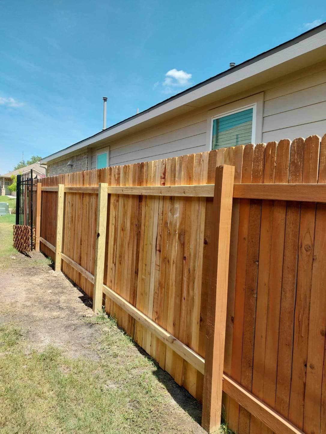 Wooden privacy fence along a house beside a grassy yard under a blue sky