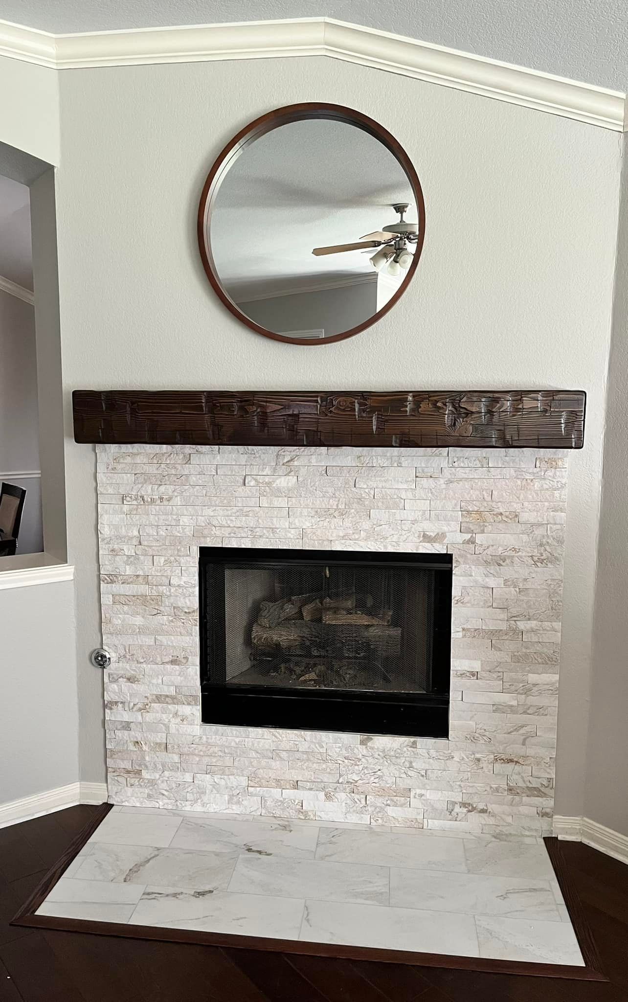 Fireplace with white stone surround, dark mantel, and round mirror above on a light gray wall.