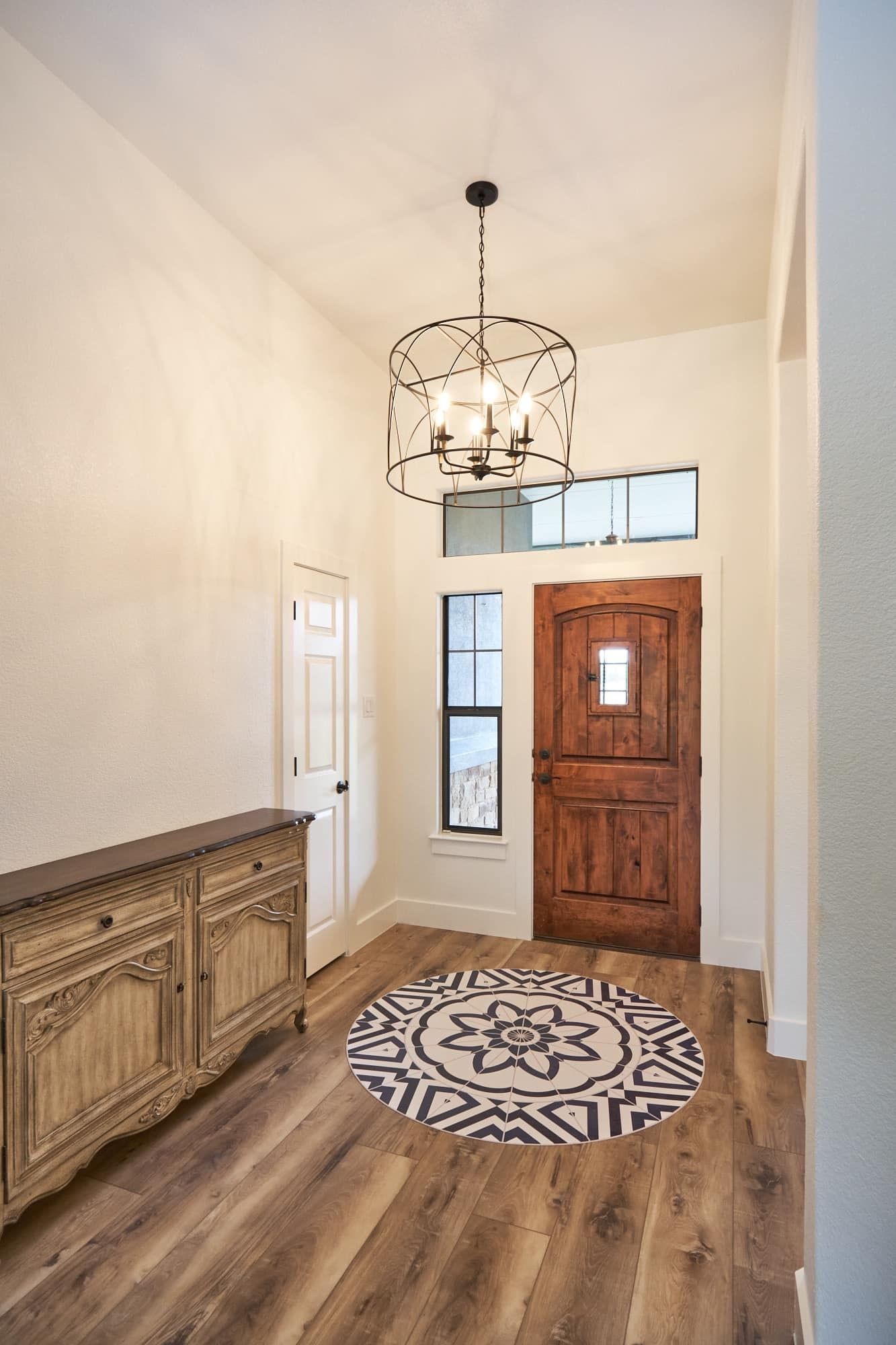 Entryway with rustic wood front door, chandelier, console cabinet, and round patterned rug on wood floor