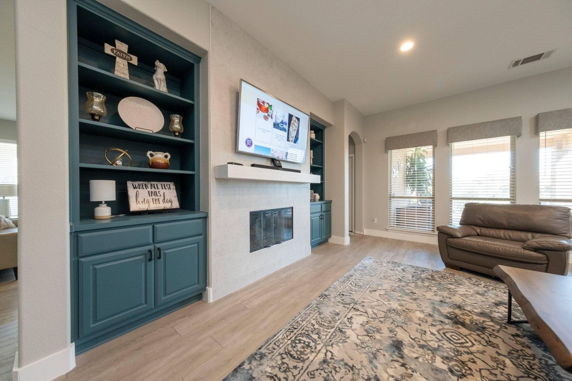 Bright living room with white fireplace, built-in shelves, wall TV, patterned rug, and brown sofa