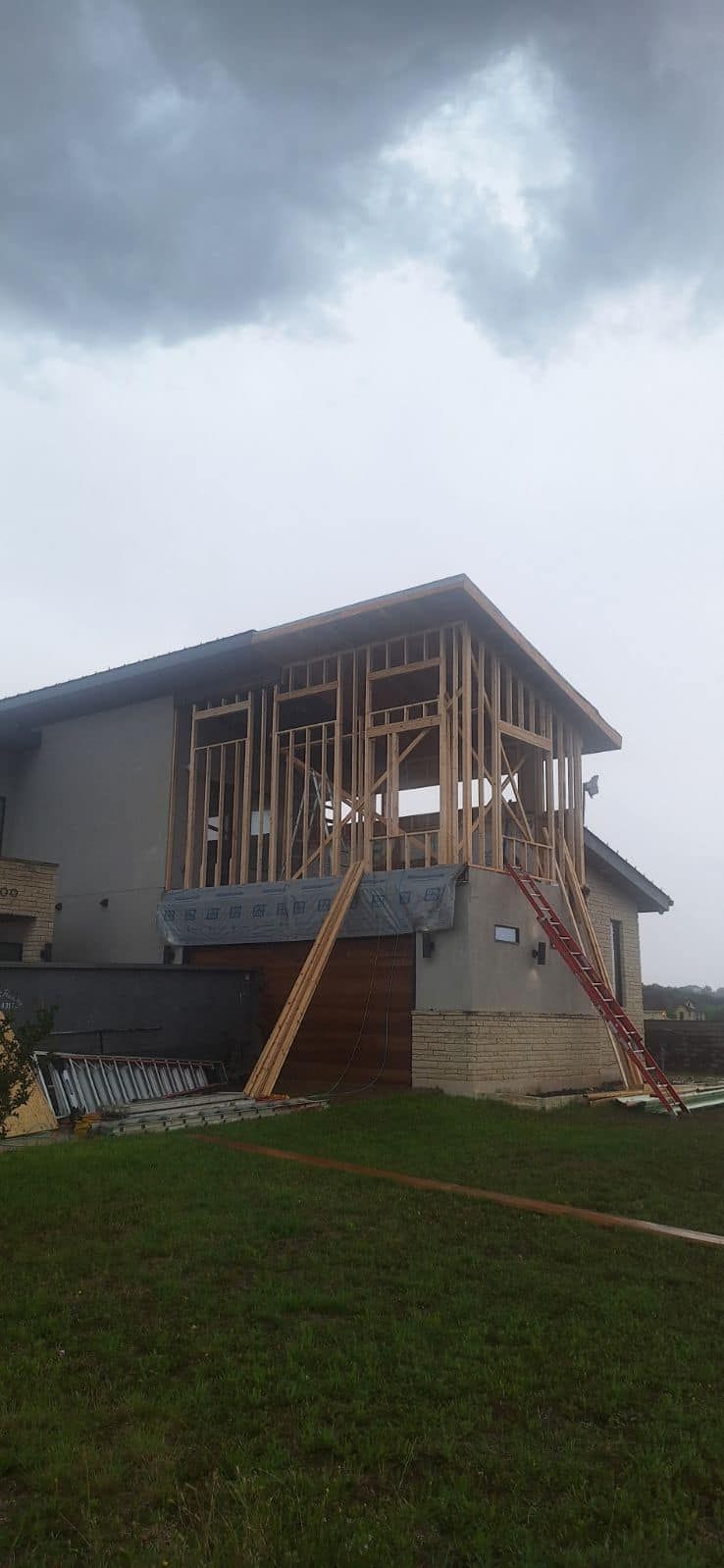 Partially built house with exposed framing under a cloudy sky on a grassy slope.